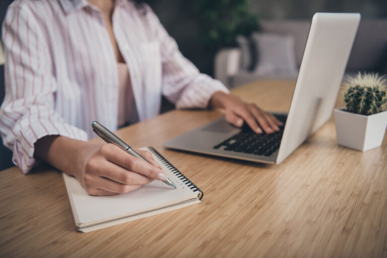 Cropped photo portrait of woman writing making list taking notes in notepad working on laptop indoors.
