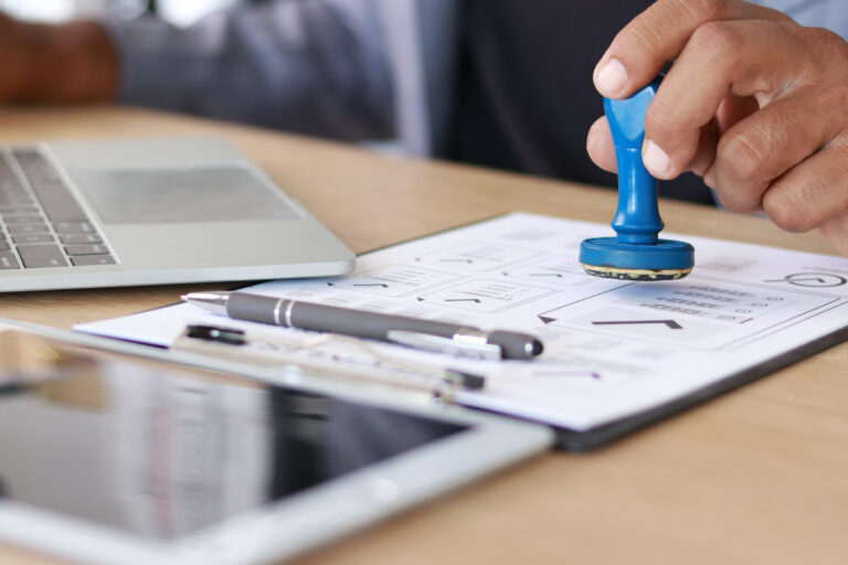 Business professional stamping approved documents on office desk with laptop and paperwork. Compliance, authorization, certification, verification, business process and corporate approval concept.